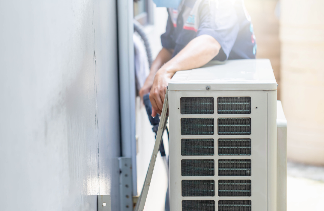 A man is installing an air conditioner on the side of a building.