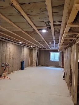 Basement under construction. Exposed wooden beams and studs, insulation, concrete floor, recessed lights.