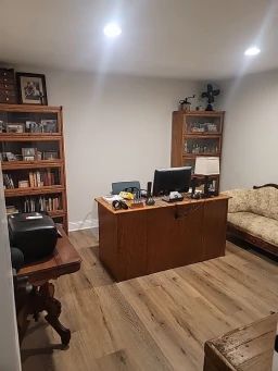 Office with wood desk, bookshelves, printer, sofa, and hardwood flooring.