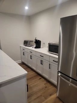 Kitchenette with white cabinets, countertop, and appliances like a toaster, coffee maker, and microwave.