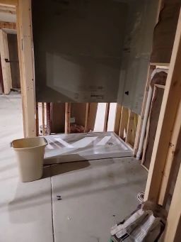 Framed bathroom under construction; shower base installed, cement board on wall. Beige bucket on floor.