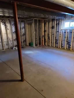 Unfinished basement with concrete floor, framed walls, insulation, and support beams.