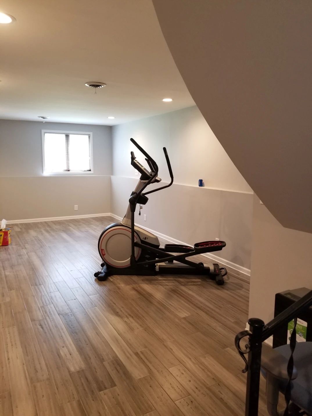Elliptical trainer in a basement gym with wood-look flooring and light gray walls.