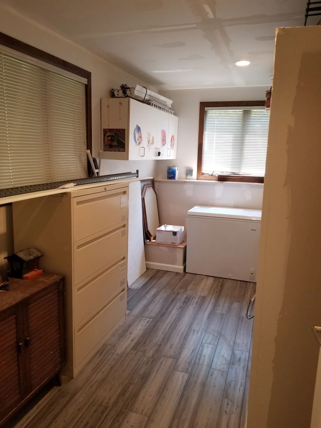 A utility room with a freezer, filing cabinet, cabinets, and a window with blinds.