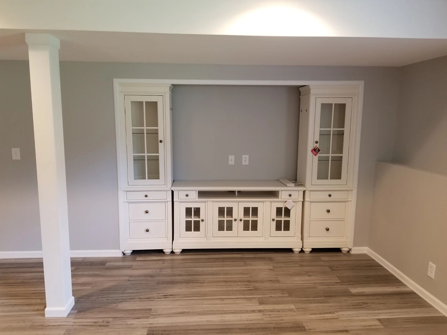 White entertainment center in a room with light gray walls, laminate flooring, and a support column.
