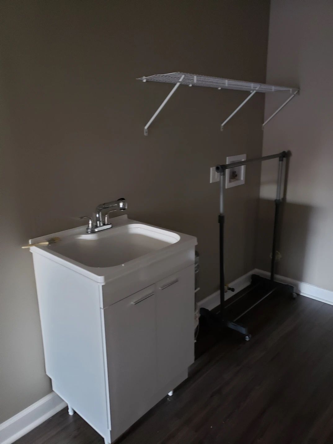 Laundry room with white sink cabinet, drying rack, and wall-mounted clothes rack.