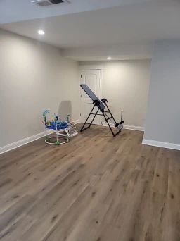 Empty room with light wood flooring, exercise equipment, and a door.