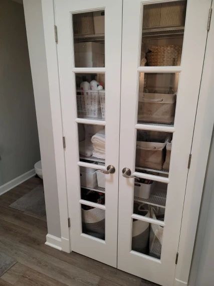 White cabinet with glass doors storing organized bathroom supplies.