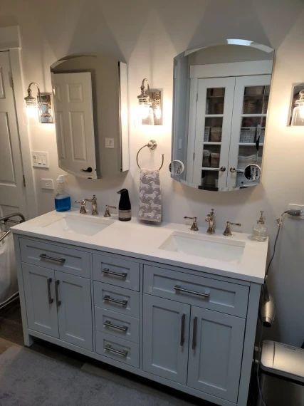 Bathroom with light blue double vanity, two mirrors, and silver fixtures.