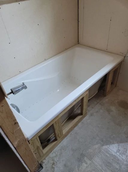 White bathtub installed in a wood frame, bathroom under construction.
