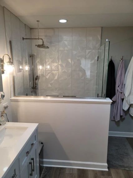 Modern bathroom with white walls, tiled shower, glass door, and white vanity.
