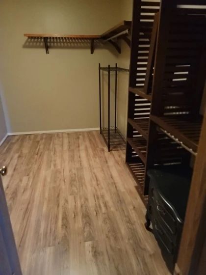Empty walk-in closet with brown shelving, a metal rack, and wood-look flooring. Beige walls.