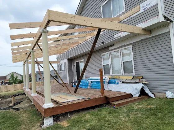 Deck construction: Wooden frame with columns, roof supports, and siding on a house.