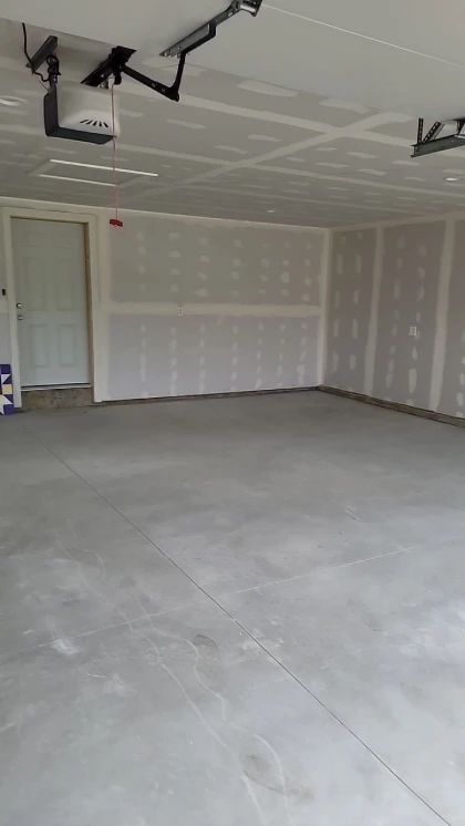 Empty garage with concrete floor, drywall walls, and a door on the left.