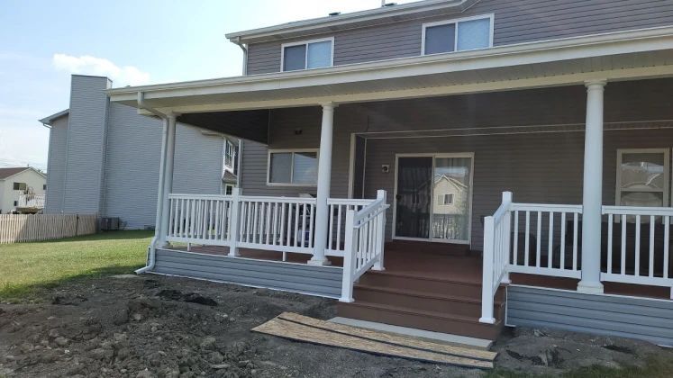 Backyard deck with white railing, brown decking, and grey siding, attached to a two-story house.
