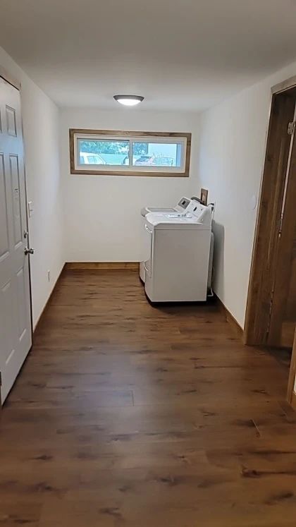 Laundry room with washer and dryer, wood floor, white walls, and a window.