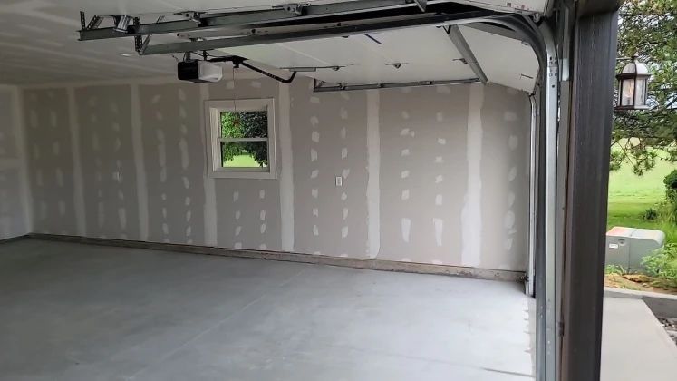 Empty garage interior, drywall installed, concrete floor, small window, open garage door.