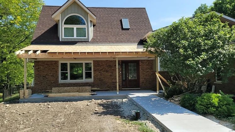 House under construction with brick exterior, brown roof, and new porch addition.