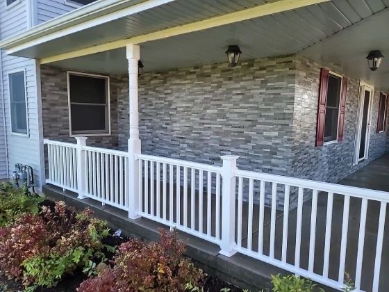 White porch railing and columns; gray stone facade; red-shuttered windows, outdoor lighting.