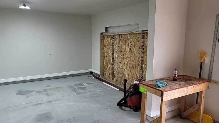 Empty garage with unfinished OSB wall, work table, and wet/dry vacuum.