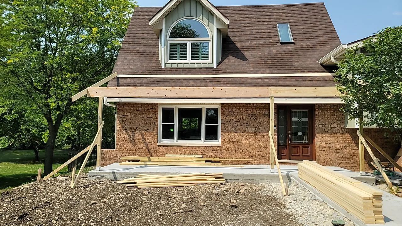 House under construction: brick exterior, wood beams for porch, with lumber and a finished brown roof.