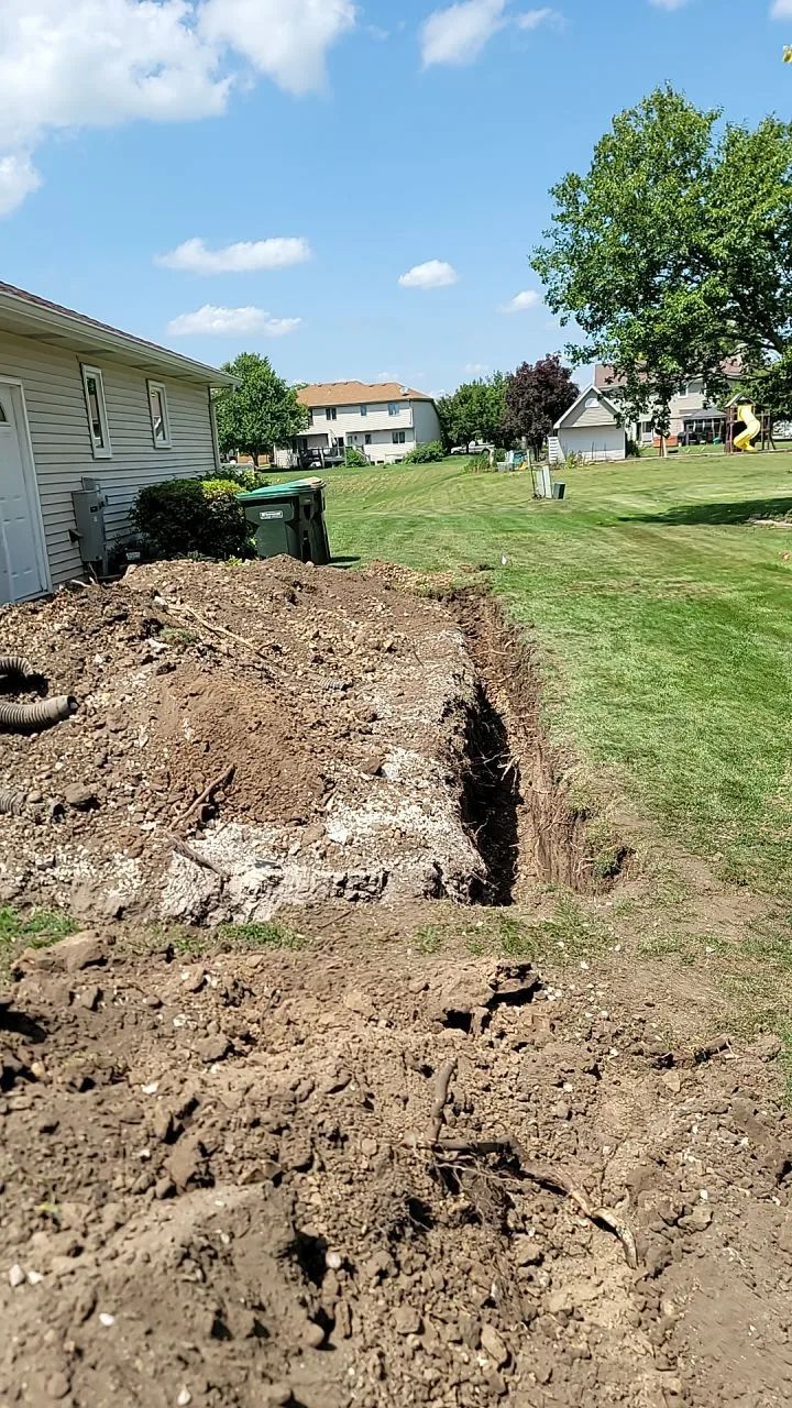 Dirt piled next to a house with a trench dug in the grass. Bright, sunny day.