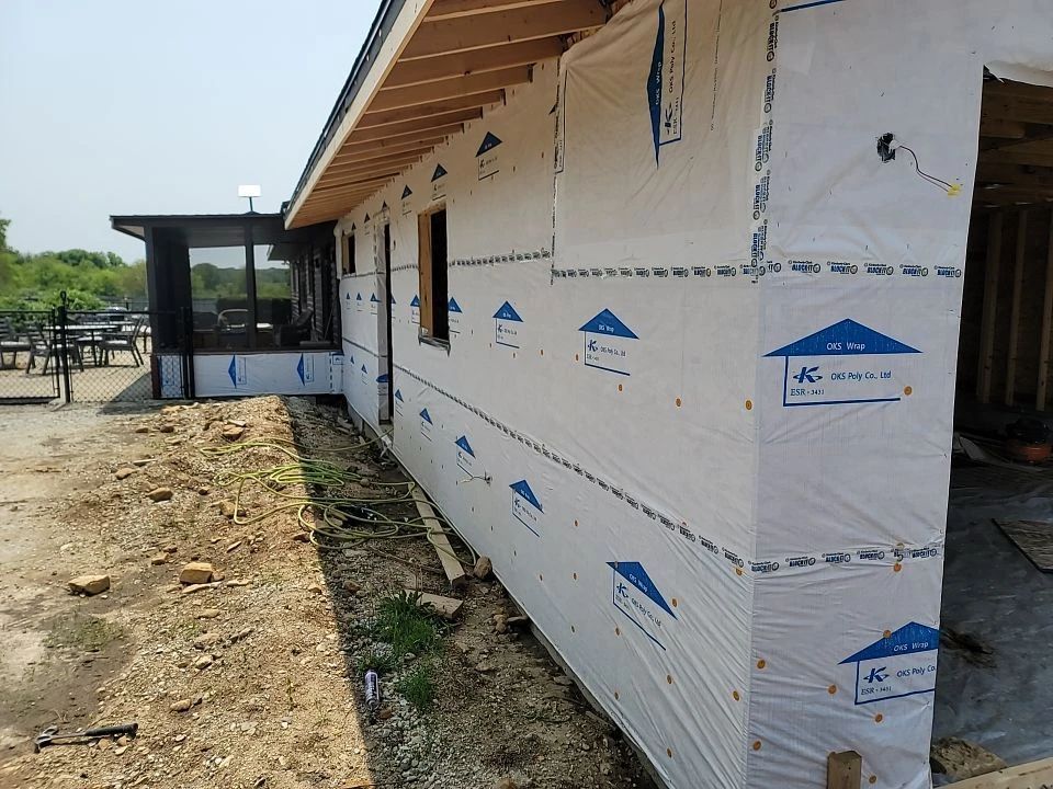 Exterior of a house under construction; white weather-resistant barrier covers walls.