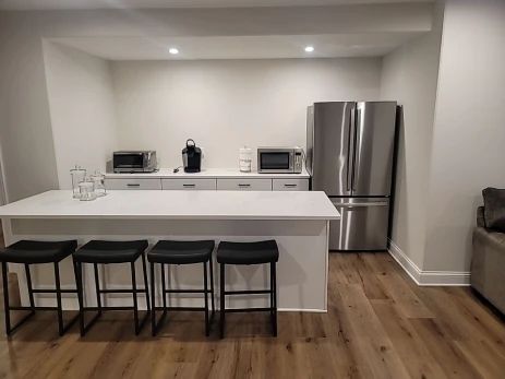 Kitchen area with a white island with bar stools, a stainless steel refrigerator, and built-in microwave and other appliances.