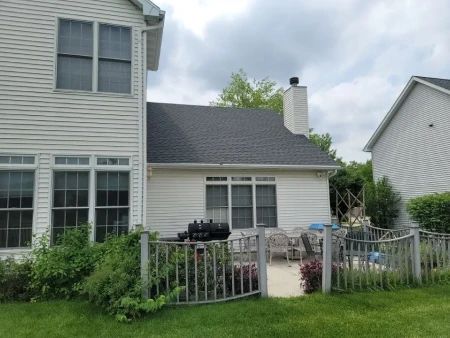 Backyard patio with wooden fence, white siding house, black grill, and overcast sky.