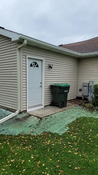 Beige house exterior with a white door, green trash bin, and grassy area.