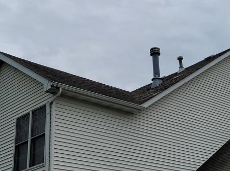 White house exterior with dark roof and two metal chimneys against a cloudy sky.