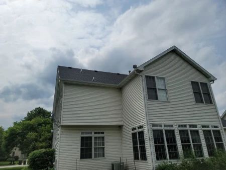Two-story house with light siding and a dark roof under a cloudy sky.