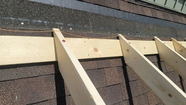 Wooden beams being attached to a roof with dark shingles.