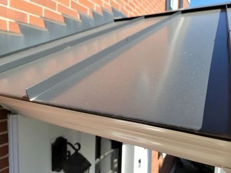 Metal awning over a door, with a gutter below, against a brick wall.