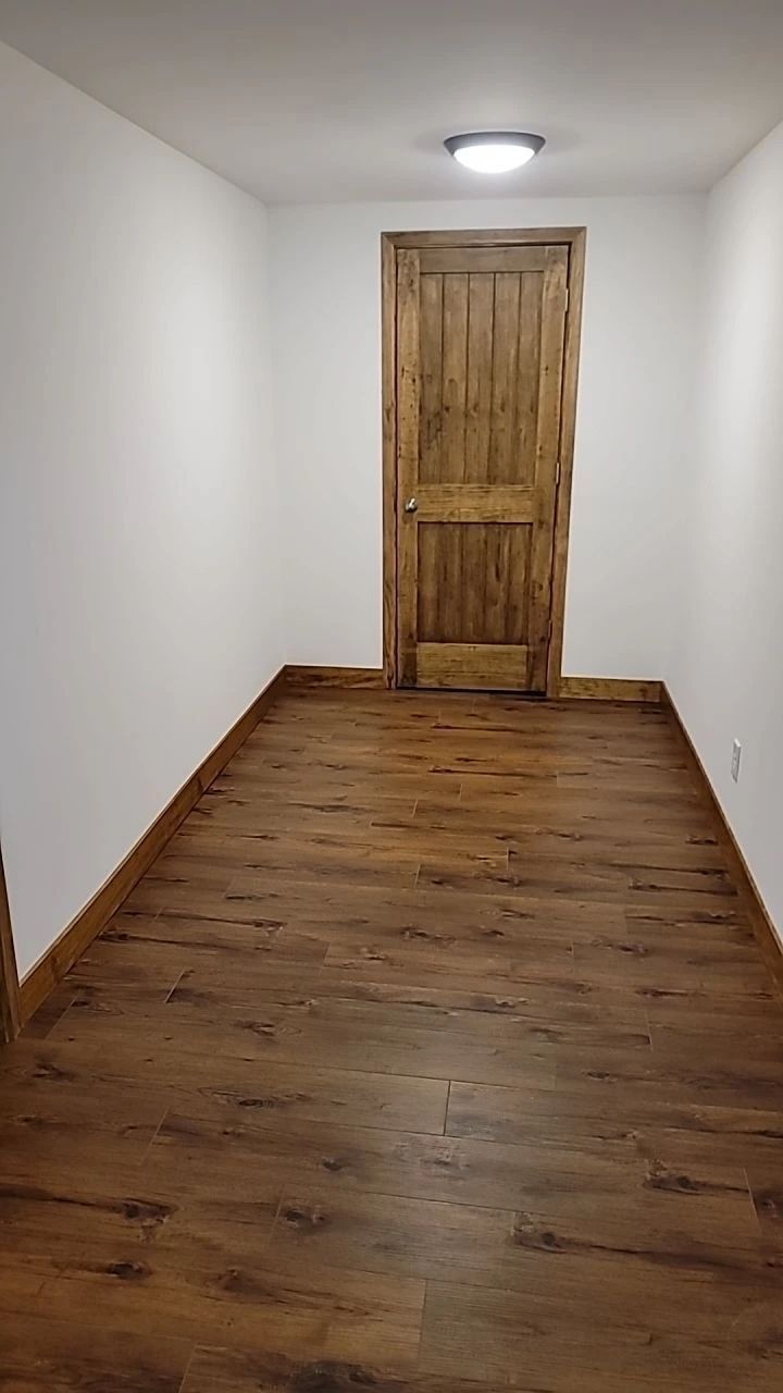 Hallway with wood flooring, white walls, wooden door, and a ceiling light.