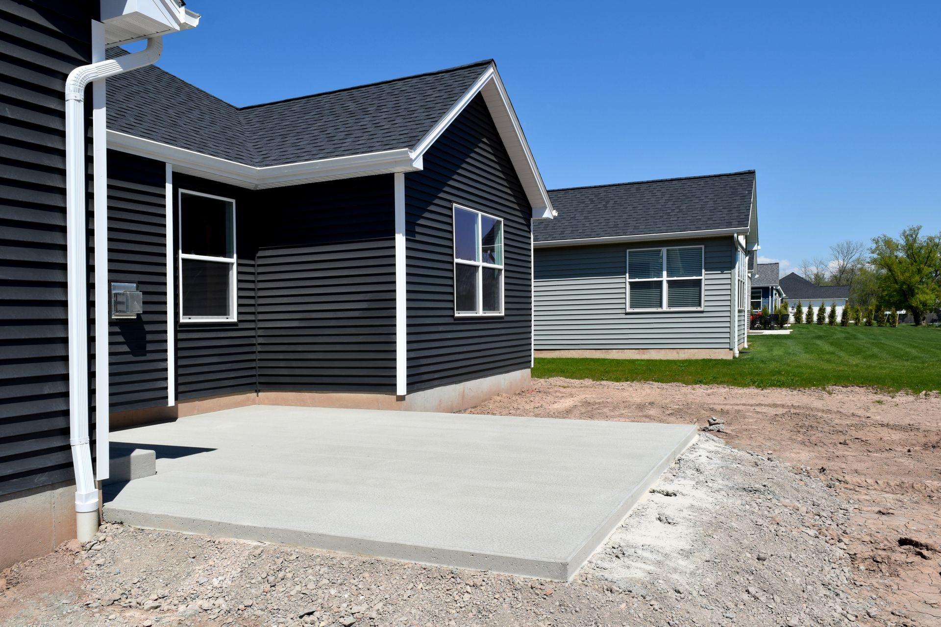 Modern house exterior with black siding, concrete patio, and gravel driveway under a blue sky