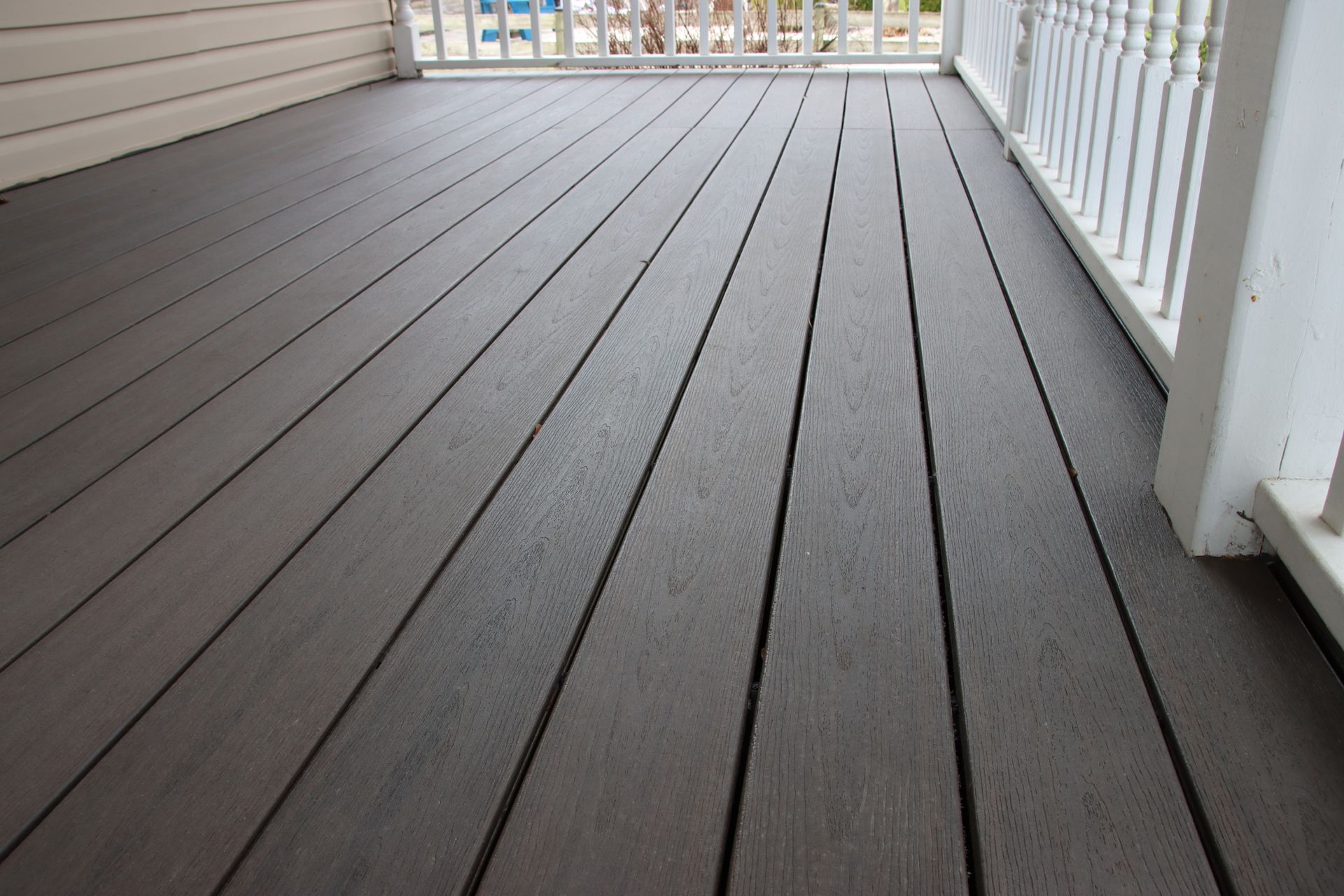 Empty gray composite deck with white railing and beige siding, viewed from a low angle