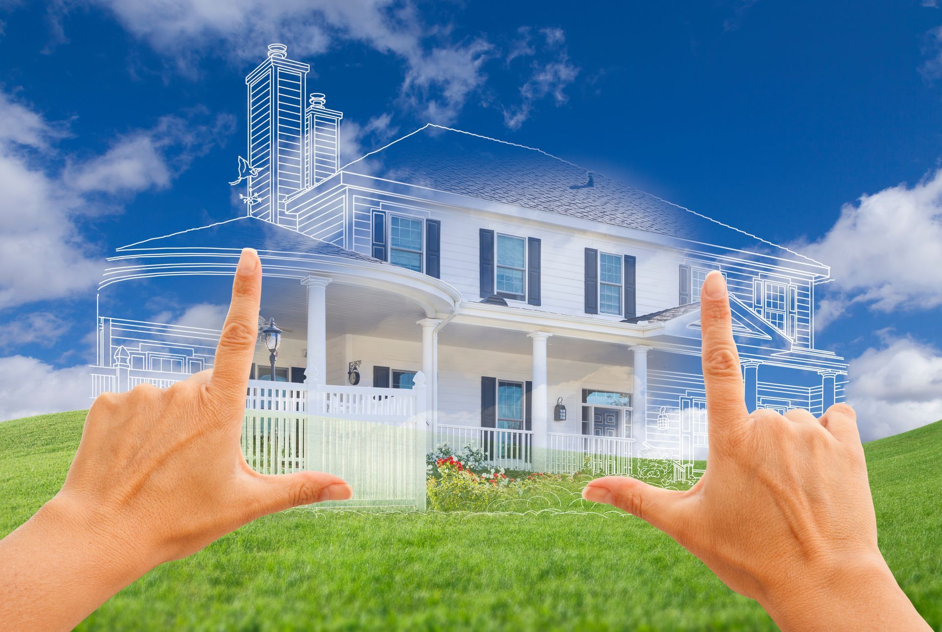 Hands framing a dream house with blueprint overlay on a grassy hill under a blue sky.