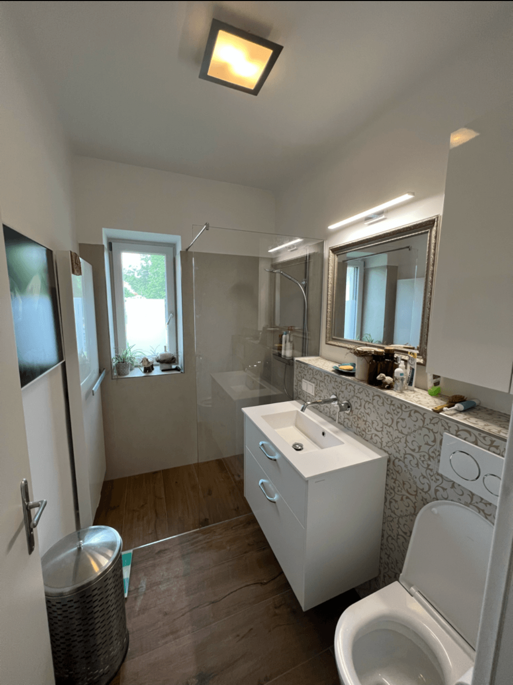 Ein Badezimmer mit Toilette, Waschbecken, Spiegel und ebenerdiger Dusche.