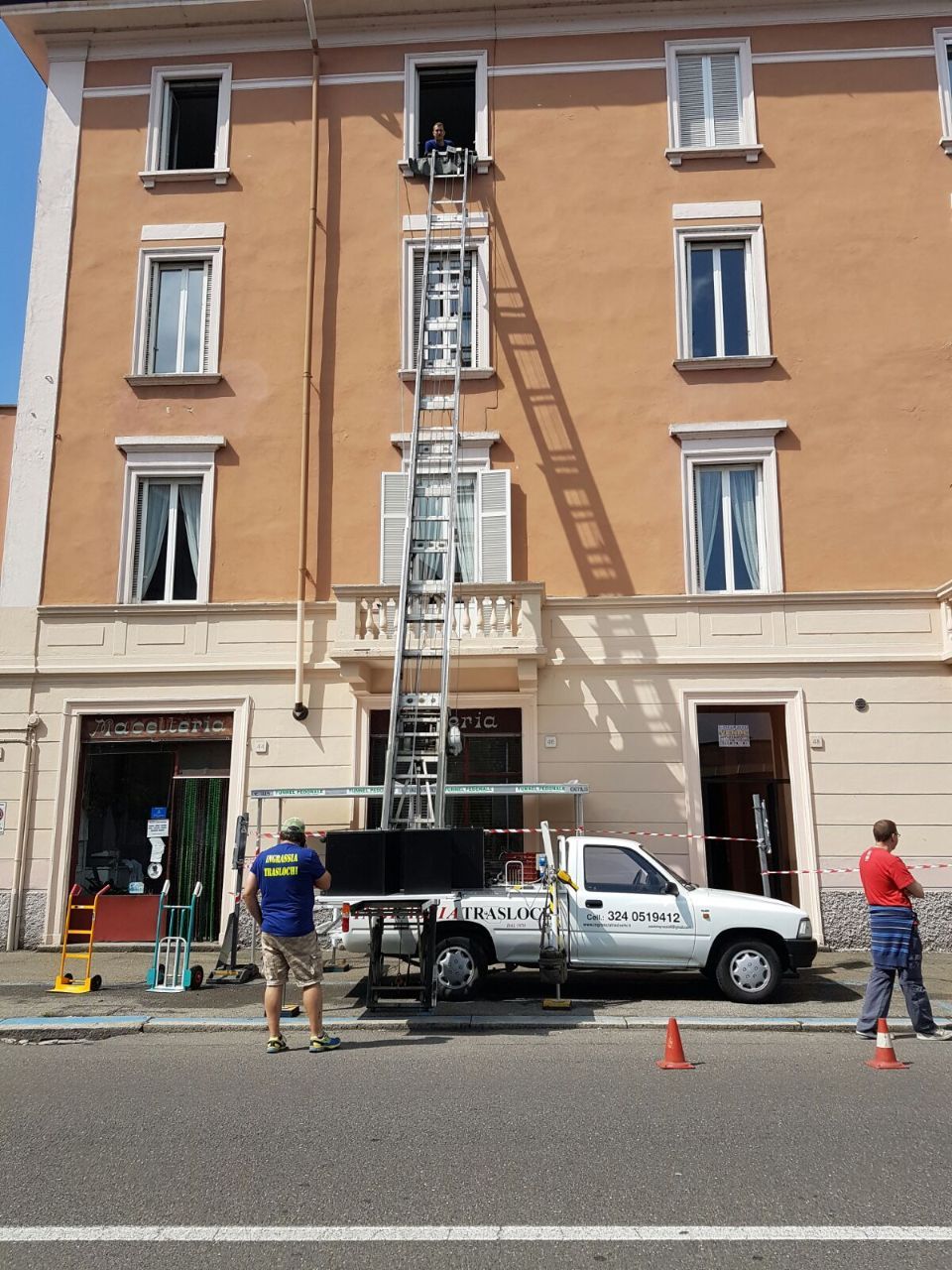 Un camion per traslochi dotato di sollevatore viene utilizzato per spostare oggetti dalla finestra superiore di un edificio. Due persone osservano.