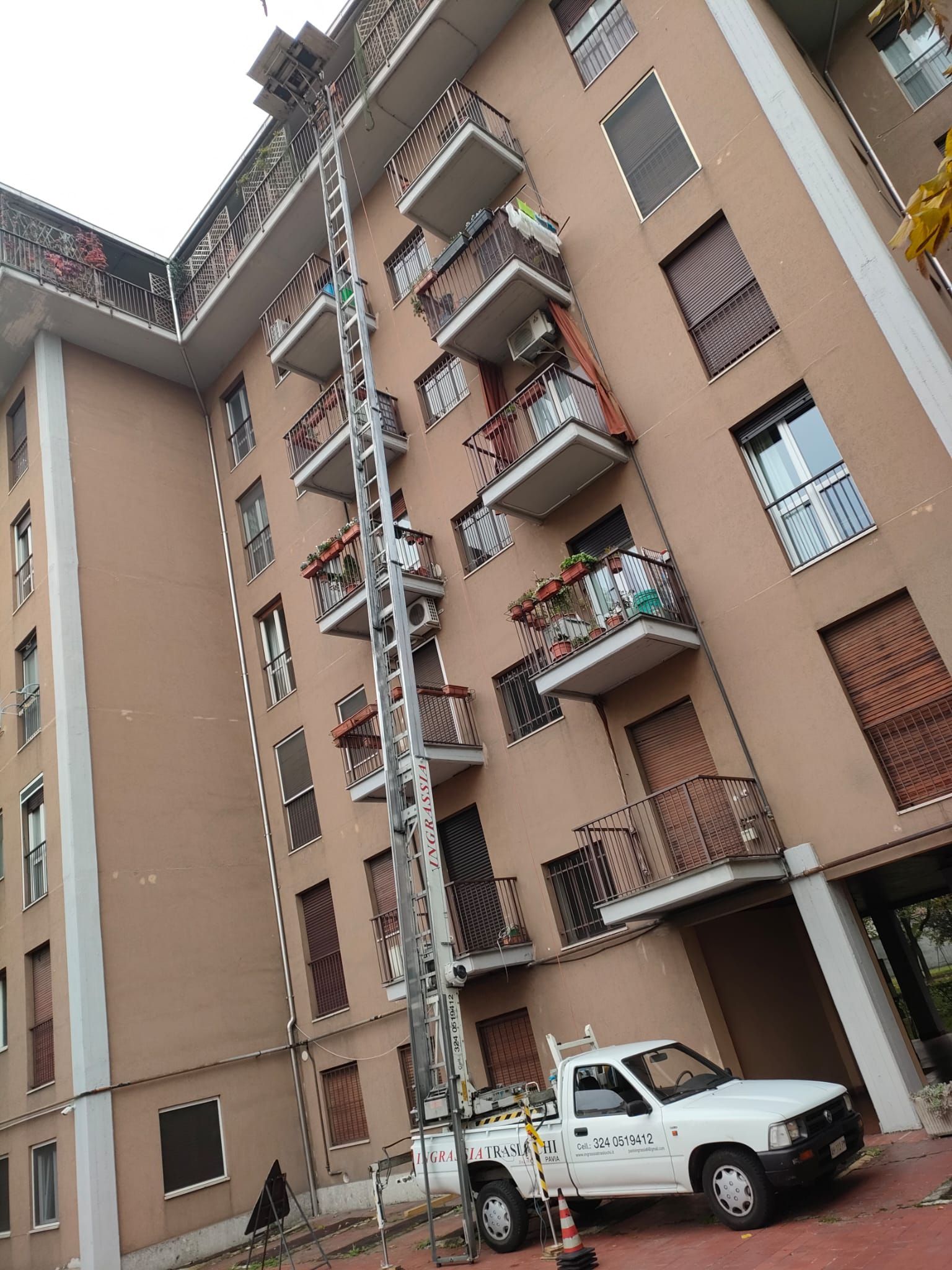 Camion con piattaforma elevatrice estesa accanto a un condominio.