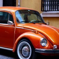 An orange VW beetle is parked in front of a yellow building.