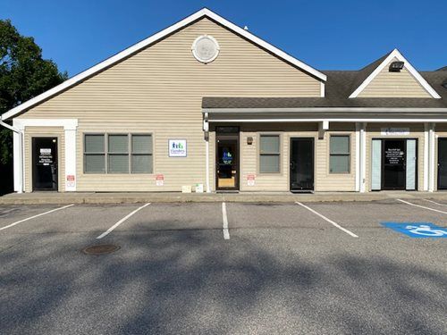 Small beige storefront with a gabled roof and empty parking lot in front