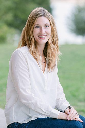 Woman in a white blouse smiling outdoors, seated against a soft green background