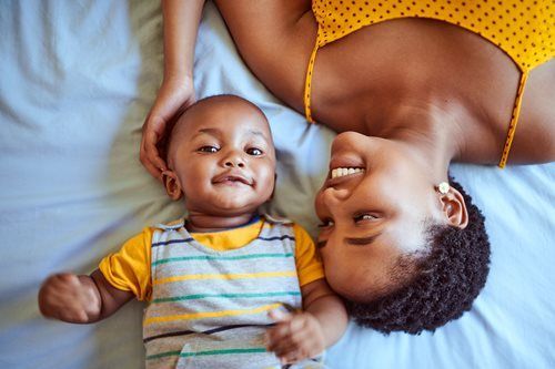 Adult and baby lying on a bed, smiling and looking at each other.