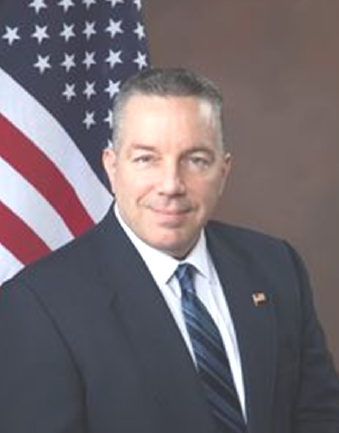 Alex Villanueva Man in suit and tie, smiling, in front of American flag, official portrait.