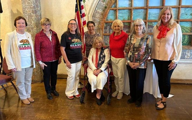 2026 Board Group of women posing, some with US flag, indoors with arched windows.