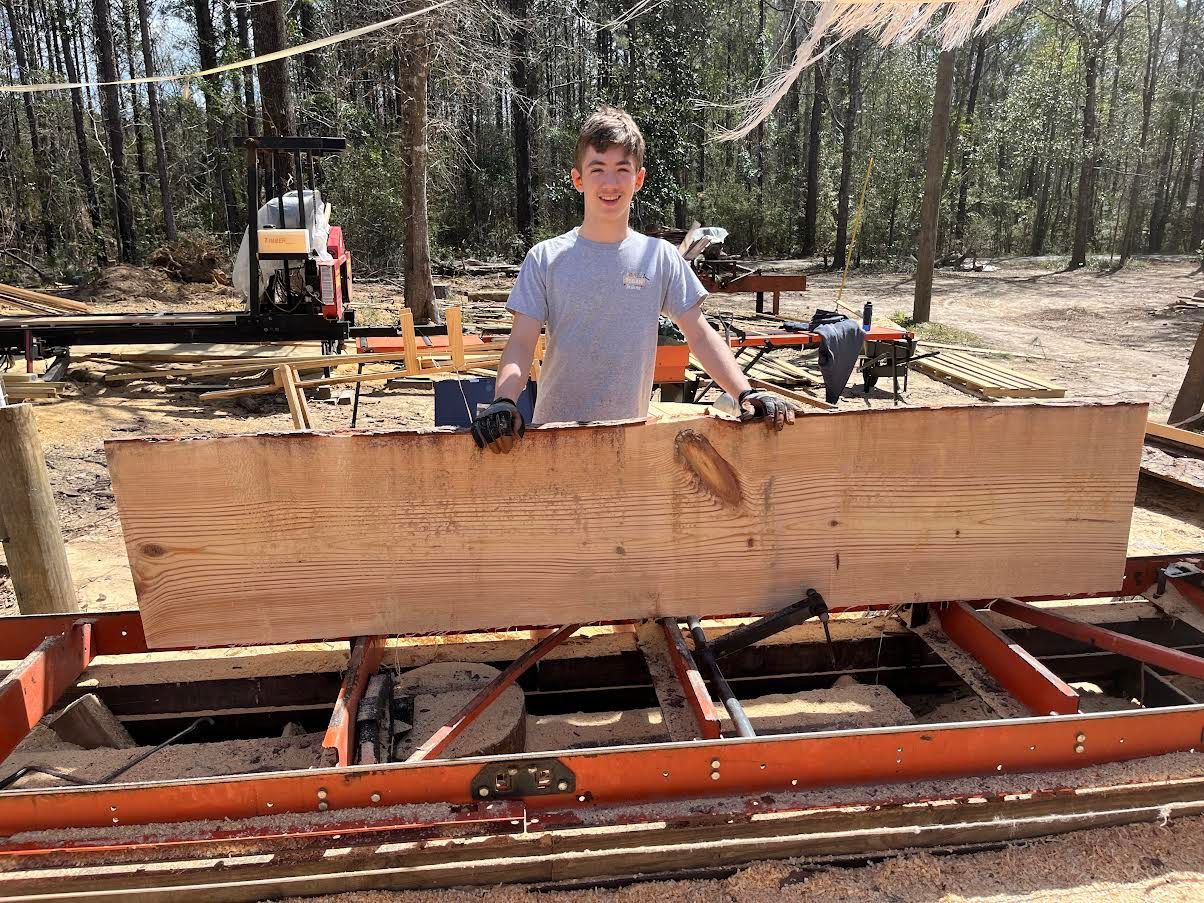 Man in apron using a plane on wood in a workshop.