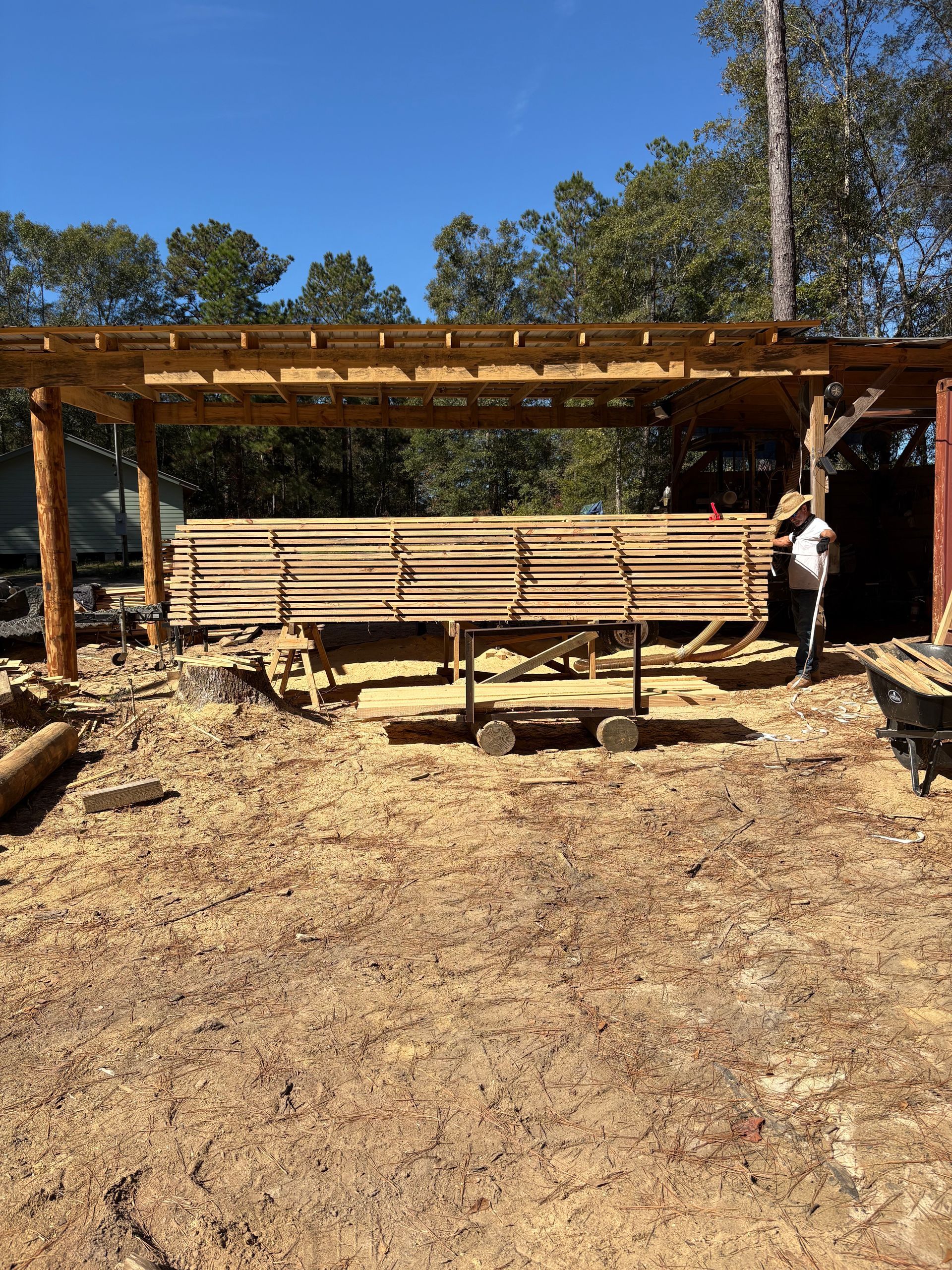 Logs piled on a weathered wooden cart in an industrial sawmill; sunlight streams through windows.
