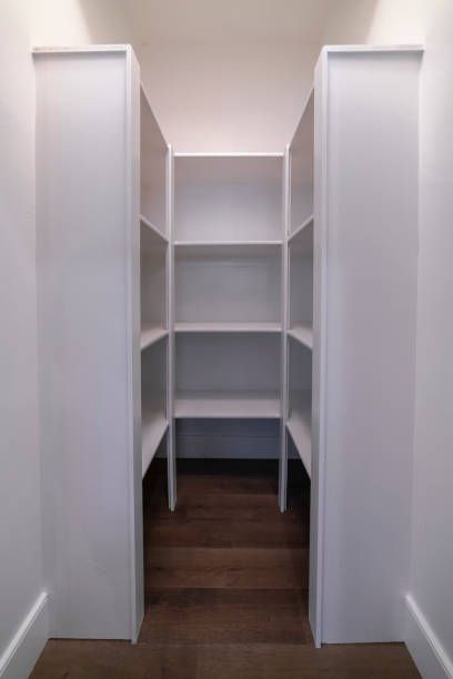 White pantry shelves recessed into a wall between two vertical white panels. Wooden floor.